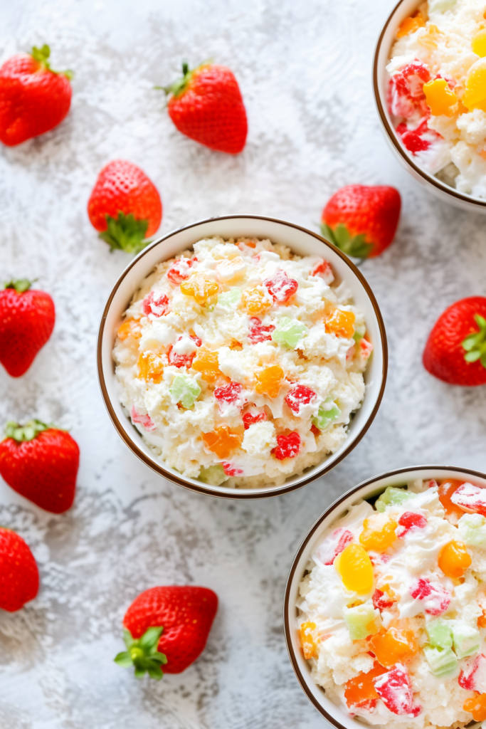 Bowl of chilled fruit salad with whipped cream and bright candied fruit.