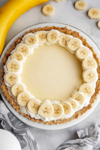 Close-up of a layered dessert with a buttery crust, creamy filling, and sliced bananas.
