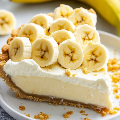 Creamy pie slice with whipped topping and banana slices, served with crumbs scattered on the plate.