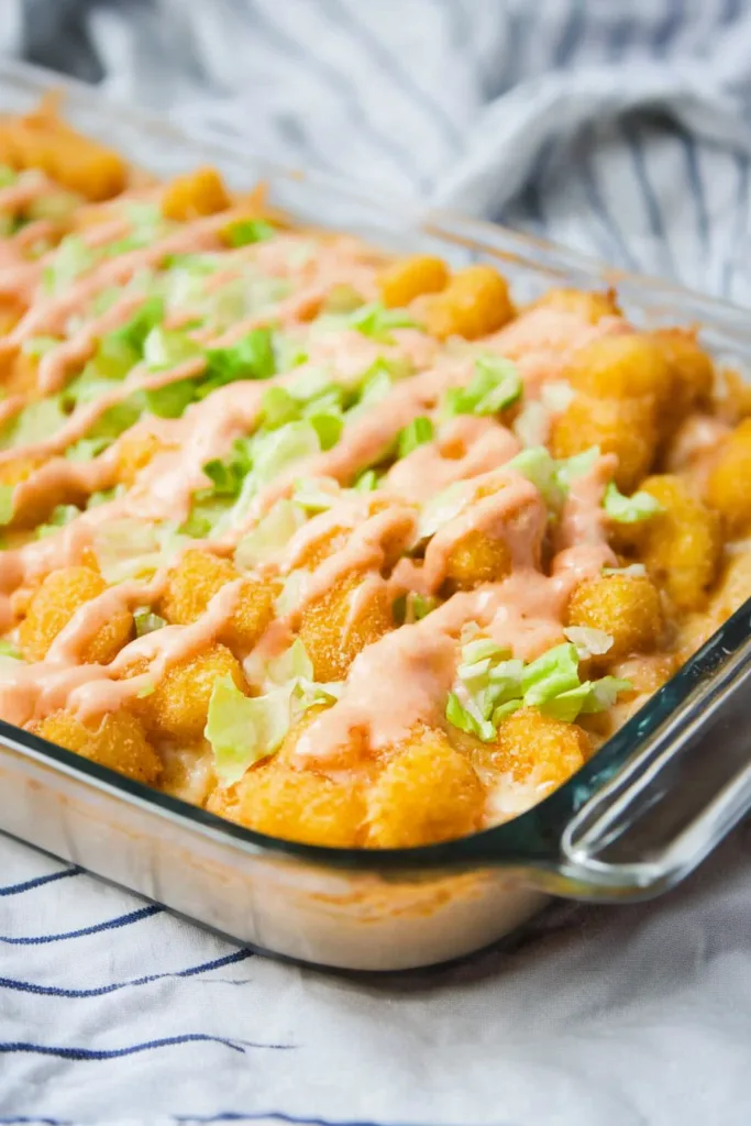 Baked tater tot dish topped with cheese, beef, and green pickle slices