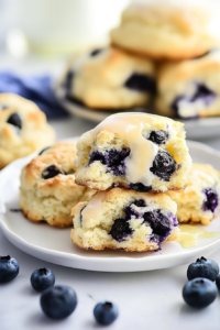Freshly baked biscuits topped with a light glaze and bursts of juicy blueberries on a white plate.