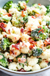 Close-up of a creamy salad with broccoli, cauliflower, and crispy bacon pieces in a white bowl.