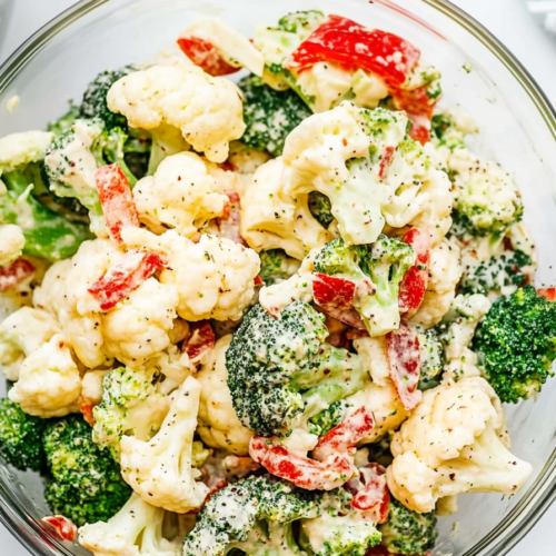 Fresh florets of broccoli and cauliflower coated in dressing, garnished with bits of smoky bacon.