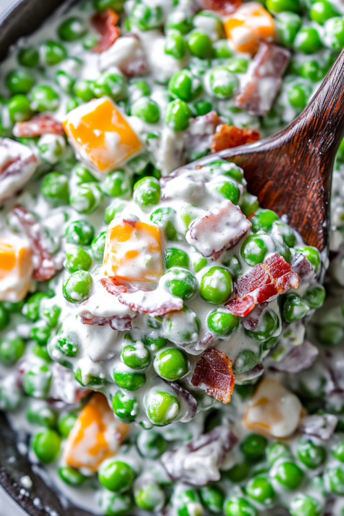 Close-up of bright green peas mixed with cheddar cubes and bacon in a creamy dressing.