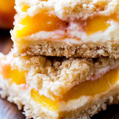 A close-up of layered dessert bars with a buttery crumb crust, creamy filling, and soft peach topping.