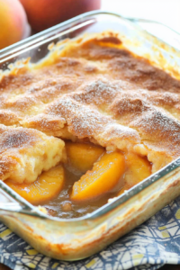 Close-up of baked dessert with a sugared top and juicy peaches visible beneath.