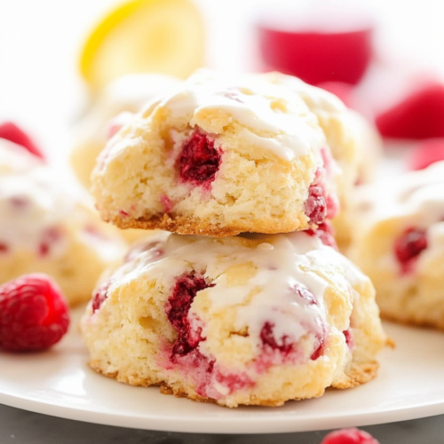 Freshly baked pastries on a white plate surrounded by bright raspberries.