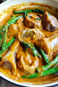 Close-up of oxtail and vegetables coated in thick peanut sauce.