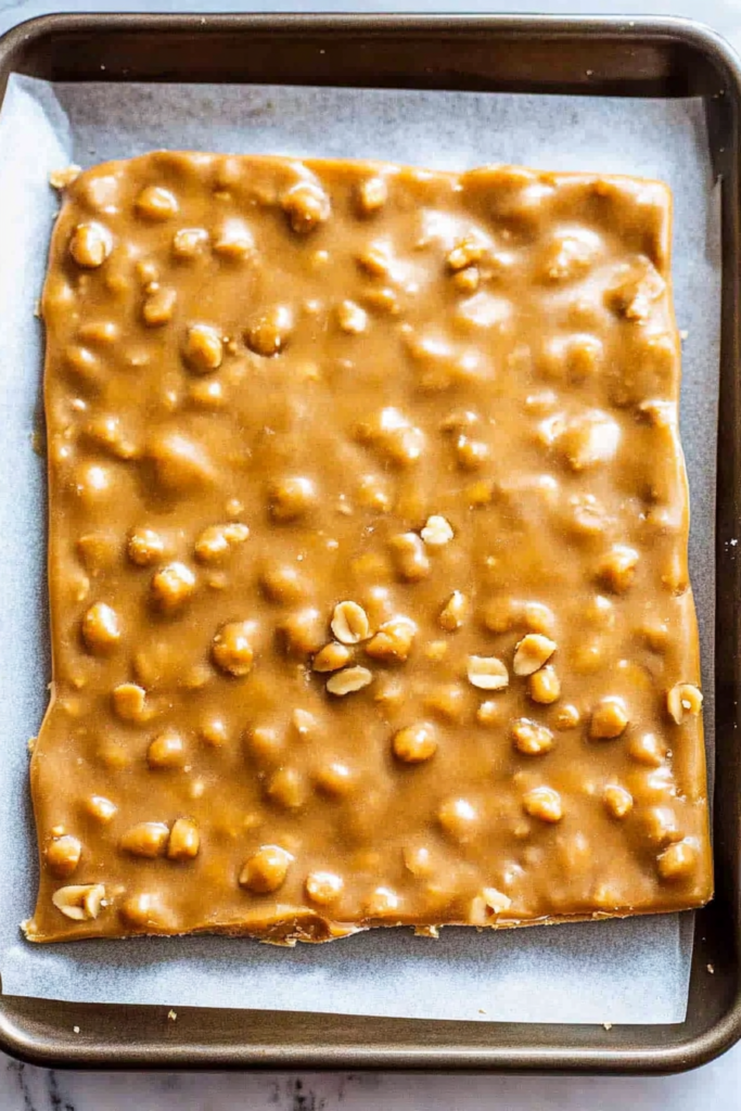 Homemade nut candy with a shiny caramel finish and visible peanuts, photographed in natural light.
