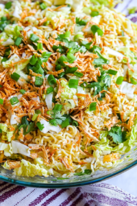 A colorful glass bowl filled with crunchy cabbage, carrots, and crispy noodles.
