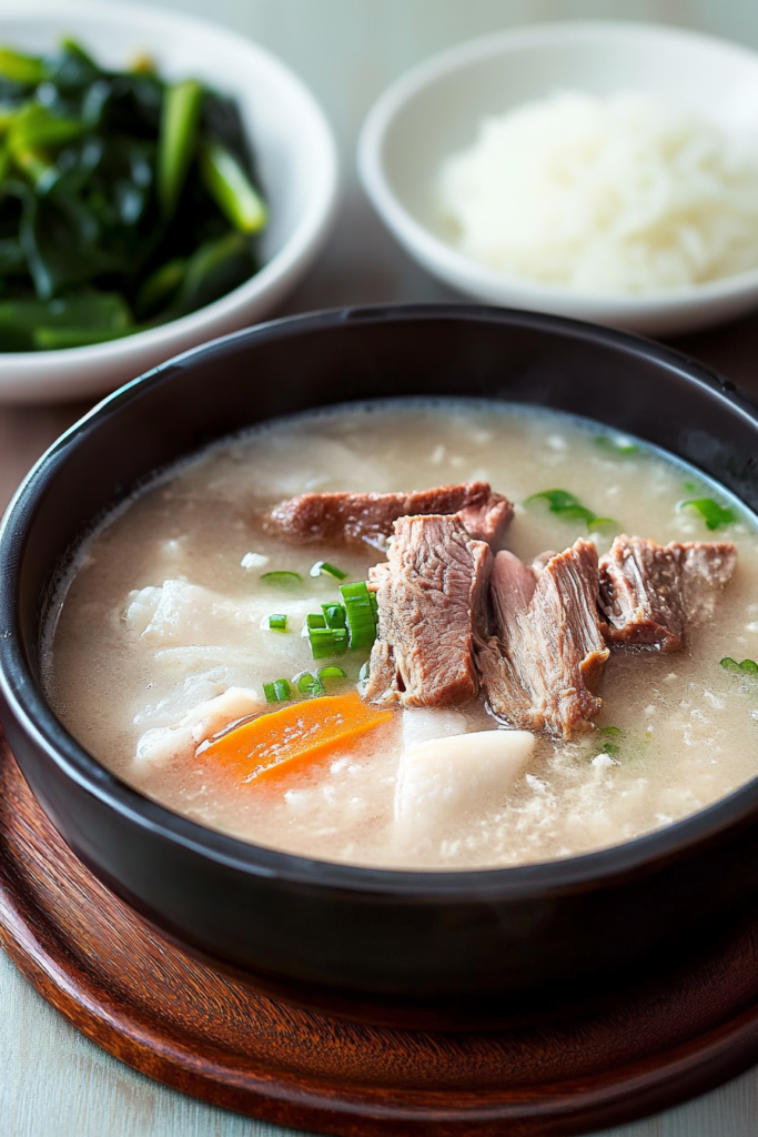 Steaming bowl of milky beef bone broth with noodles and green onions served on a wooden table.