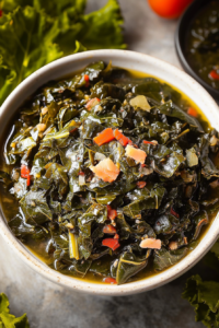 A steaming bowl of tender greens with bits of bacon and red pepper, served rustic-style.