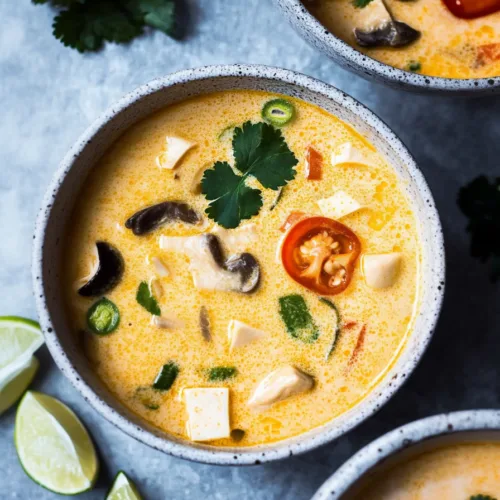 Bowl of dairy-free coconut soup topped with cilantro, tofu cubes, and Asian mushrooms.