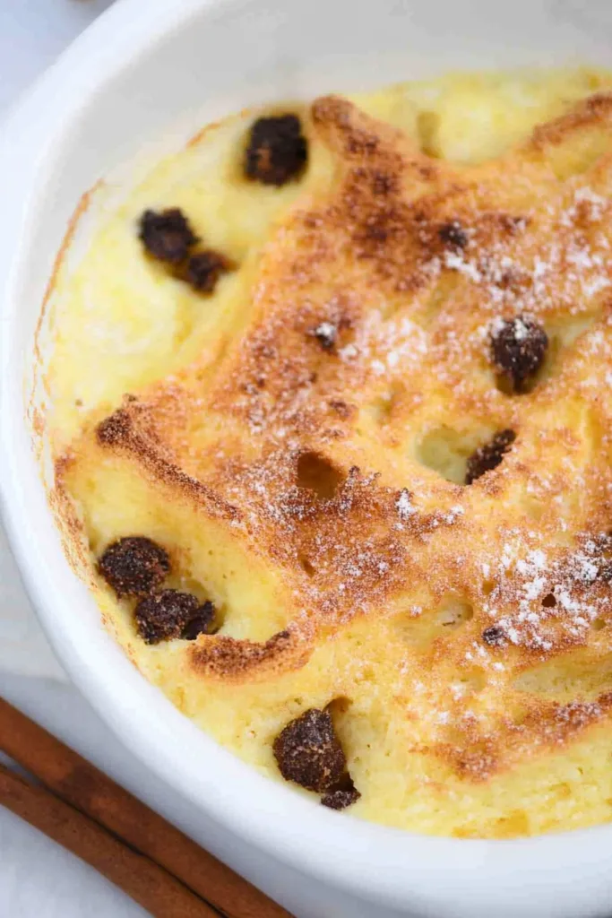Close-up of warm bread pudding topped with a crisp surface and scattered dried fruit.