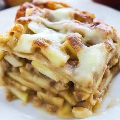 Golden-baked layered cinnamon rolls with apples cooling in a casserole dish on a rustic wooden table