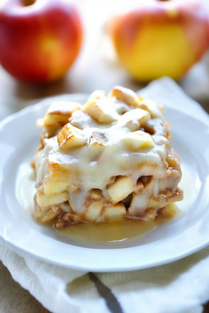 A plated dessert slice showing gooey apple filling and cinnamon roll layers topped with caramel glaze