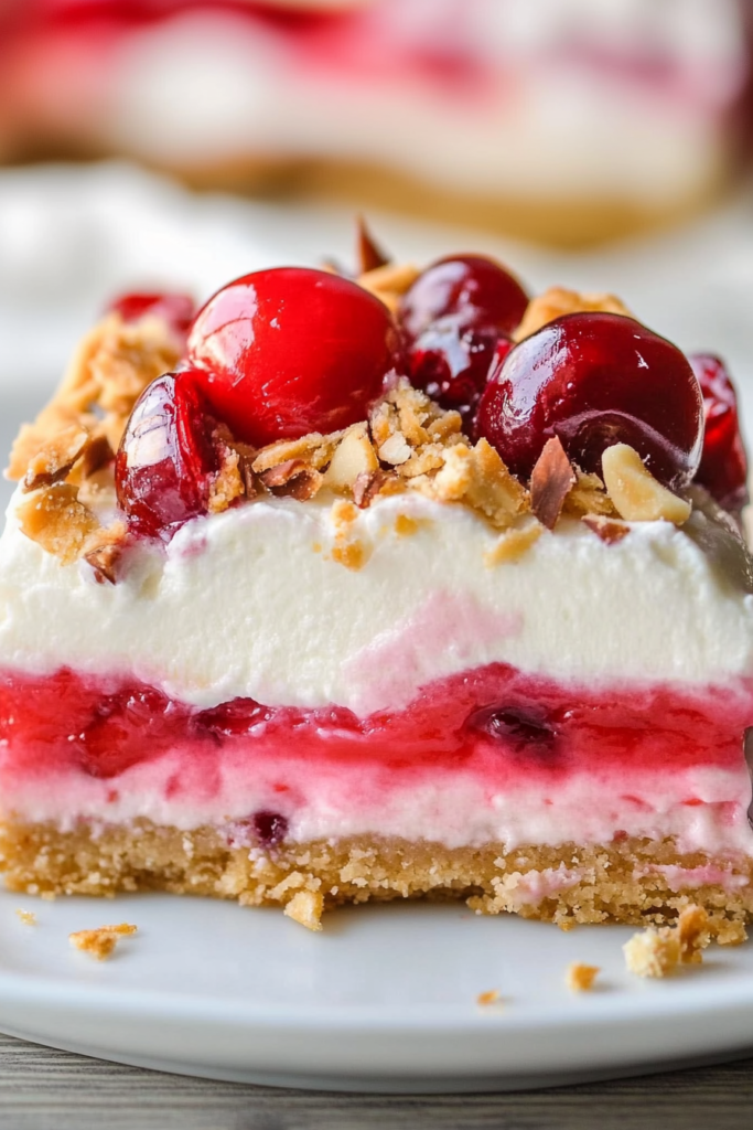 A chilled dessert bar with layers of whipped cream, cherry topping, and graham crust on a white plate.