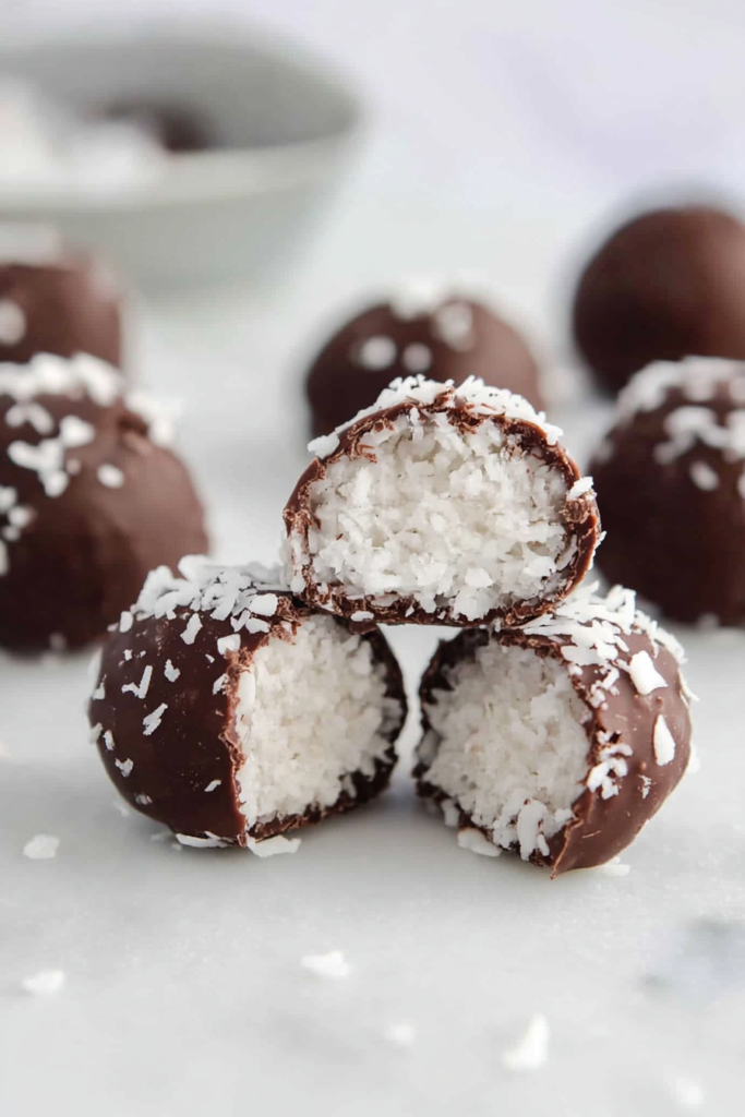 Chocolate-covered coconut bites with a soft white center, stacked and ready to serve.