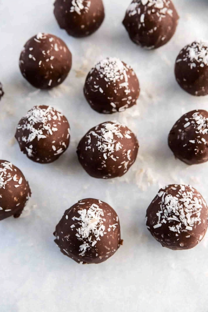 Homemade coconut dessert balls dipped in chocolate and sprinkled with coconut flakes.