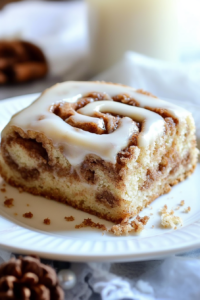 Glazed cinnamon-filled cake piece served on a plate with crumbs around the edge.