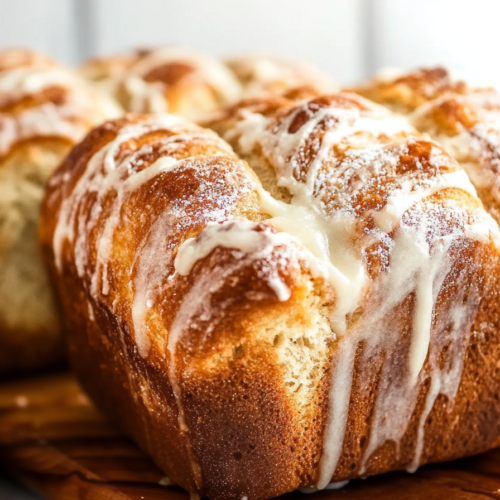 Baked sweet bread cooling on a wooden board with icing dripping down the sides.