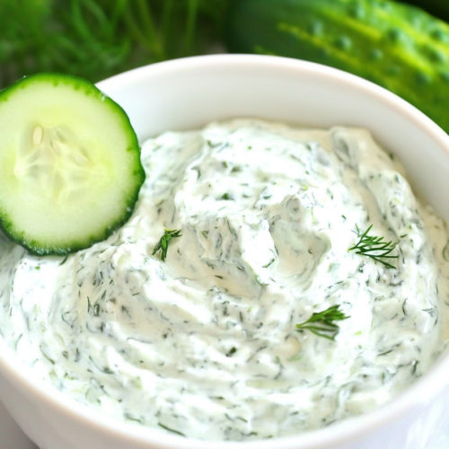 Smooth yogurt-based dip garnished with thinly sliced cucumbers.