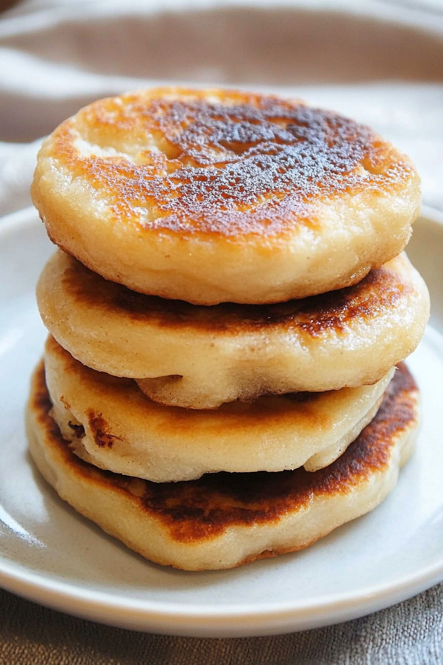 Close-up of golden-brown pancakes stacked on a white plate, showing crisp edges and fluffy texture.