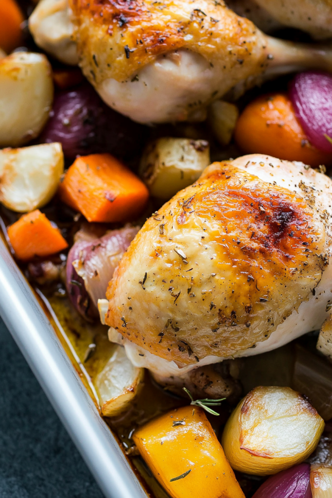 Baked chicken pieces surrounded by browned onions, carrots, and potatoes.