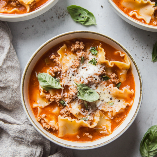 Top-down view of a rustic red broth with melted cheese and torn pasta sheets.