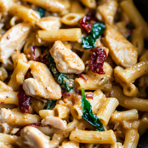 Close-up of creamy penne pasta with chicken, spinach, and sun-dried tomatoes in a rich sauce.