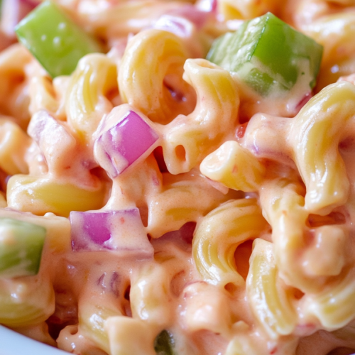 Close-up of curly pasta tossed in a smooth, rosy sauce with fresh vegetables.