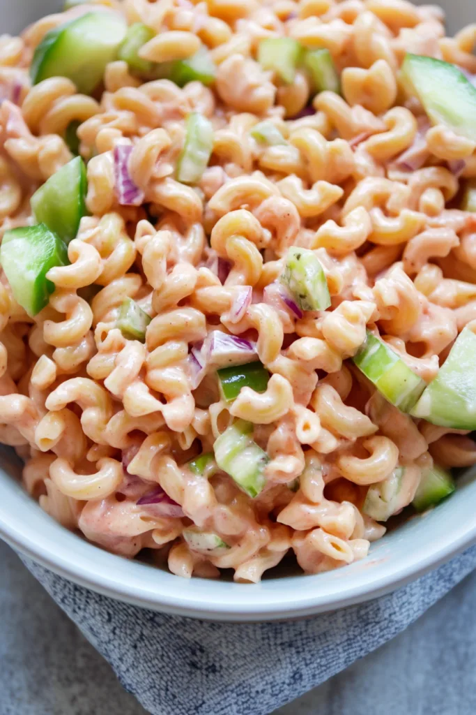 Bowl of chilled pasta salad featuring a tangy pink dressing and crisp vegetables.
