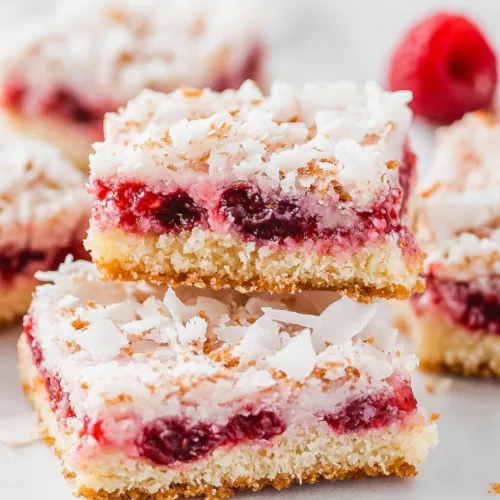 Freshly baked dessert bars with a vibrant raspberry layer and lightly toasted coconut surface.