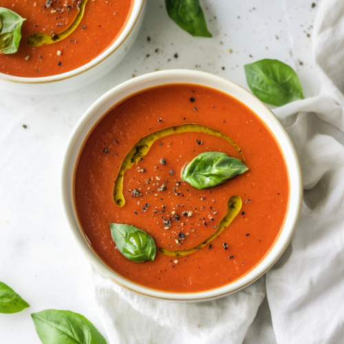 Rich red tomato soup finished with basil leaves and olive oil in a ceramic bowl