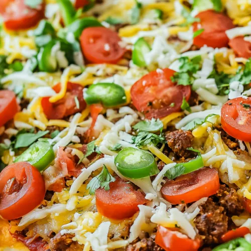 Close-up of a fully baked pizza covered with taco-style toppings and fresh herbs.