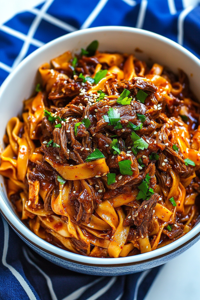 Savory beef and noodles coated in rich sauce, garnished with fresh scallions and sesame.