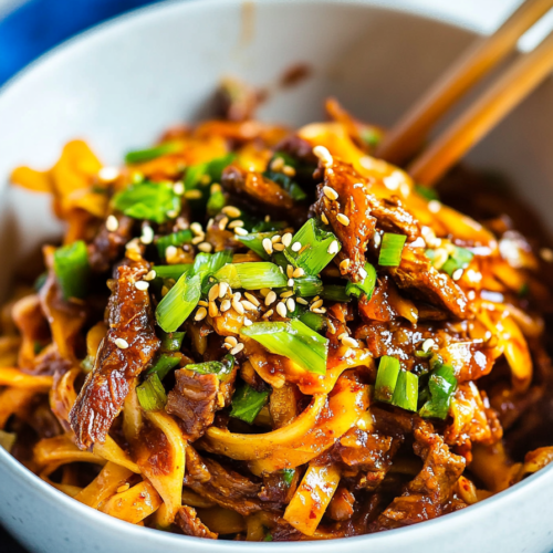 Close-up of saucy noodles and beef, glistening under a sprinkle of sesame seeds.