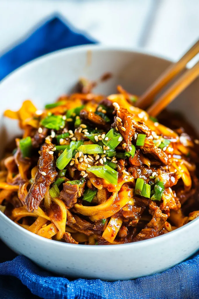 Close-up of saucy noodles and beef, glistening under a sprinkle of sesame seeds.