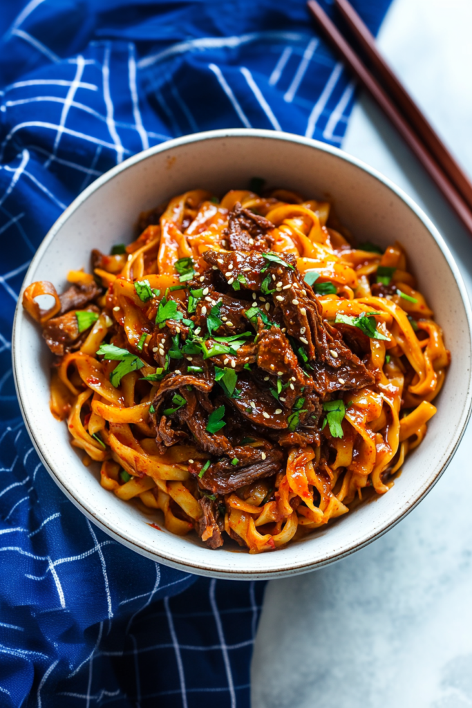 Comforting noodle dish with sliced beef and scallions, served in a deep bowl on a blue cloth.