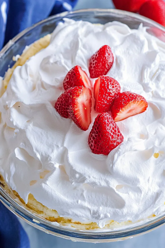 Layered dessert in a glass bowl with sponge cake, whipped cream, and fresh strawberries on top.