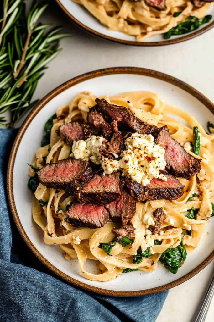 Plate of pasta with seared steak and crumbled cheese garnish.