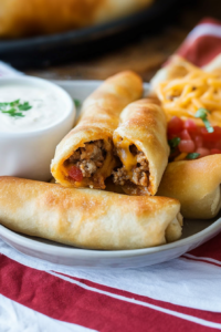 Final plated shot of stuffed cheesy taco sticks, paired with a bowl of marinara sauce.
