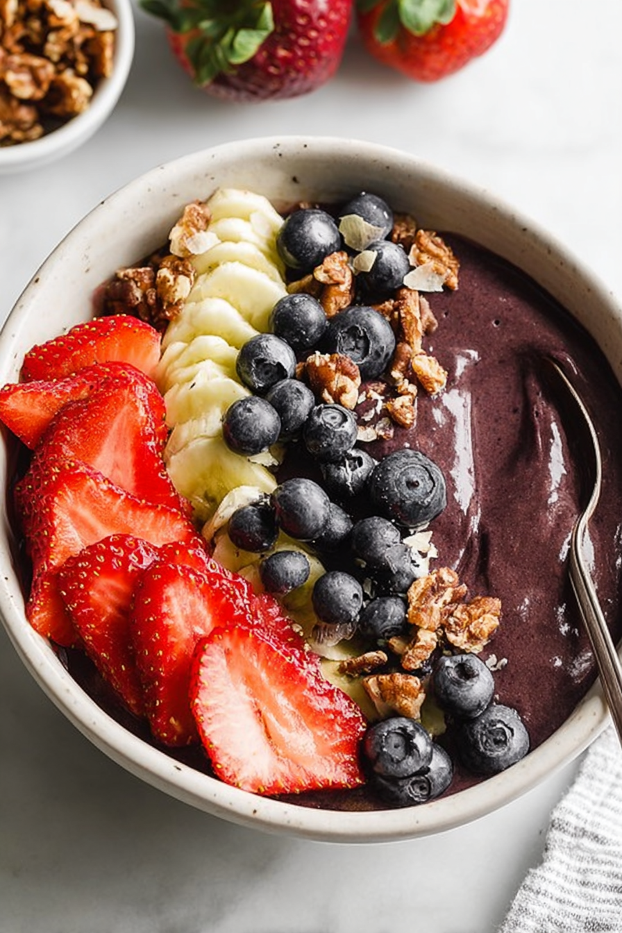 Smooth berry bowl topped with sliced strawberries, banana, blueberries, and chopped nuts.