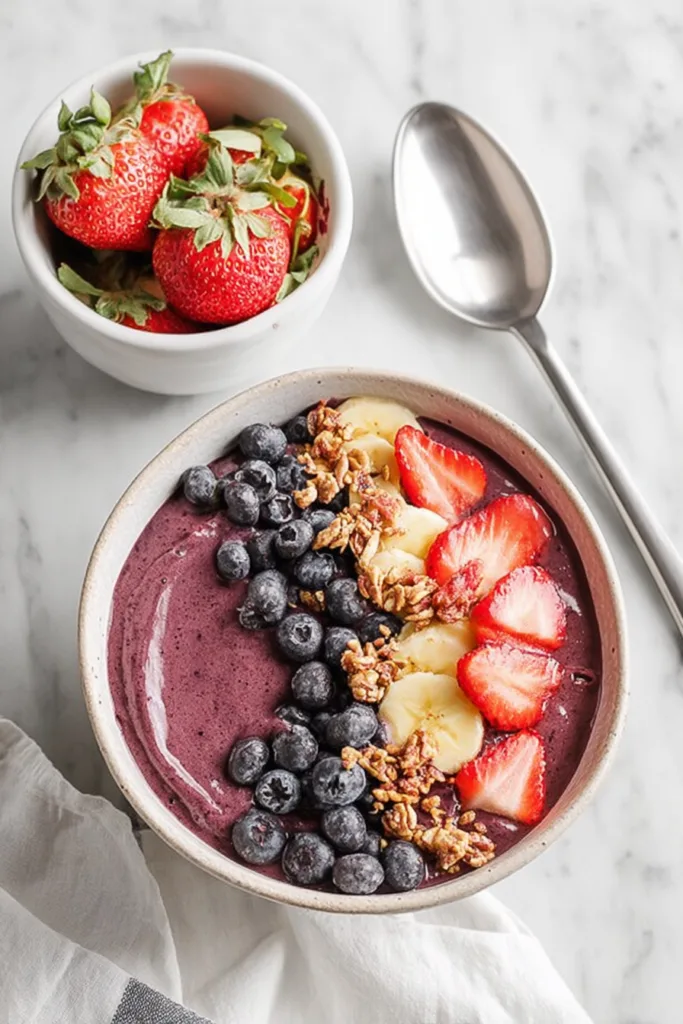 Fresh fruit bowl with layered toppings and a spoon ready for serving.