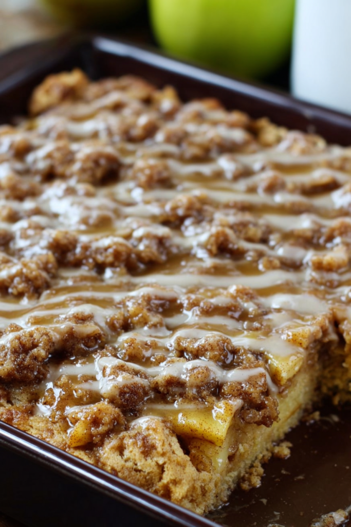 Whole crumble-topped cake on a serving board, surrounded by fresh apples in the background.