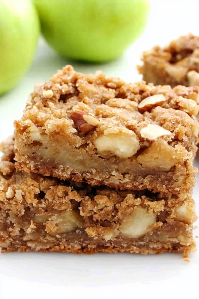 Close-up of buttery dessert bars filled with tender apple pieces and chopped walnuts.