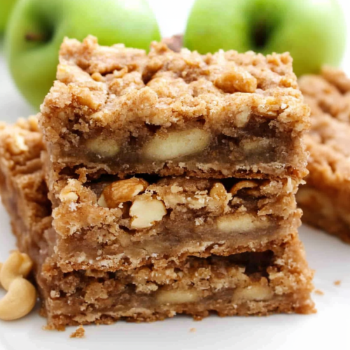 Golden brown apple crumb bars stacked on a white plate with fresh green apples in the background.