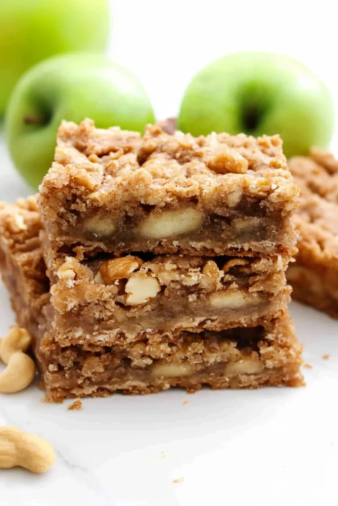 Golden brown apple crumb bars stacked on a white plate with fresh green apples in the background.