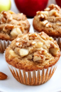 Close-up of moist spiced muffins with a nutty topping, fresh apples in the background.