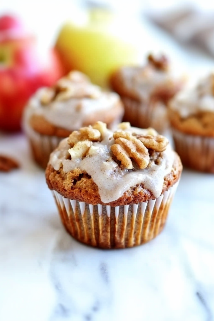Golden-brown muffins in paper liners, topped with chopped walnuts and apple pieces.